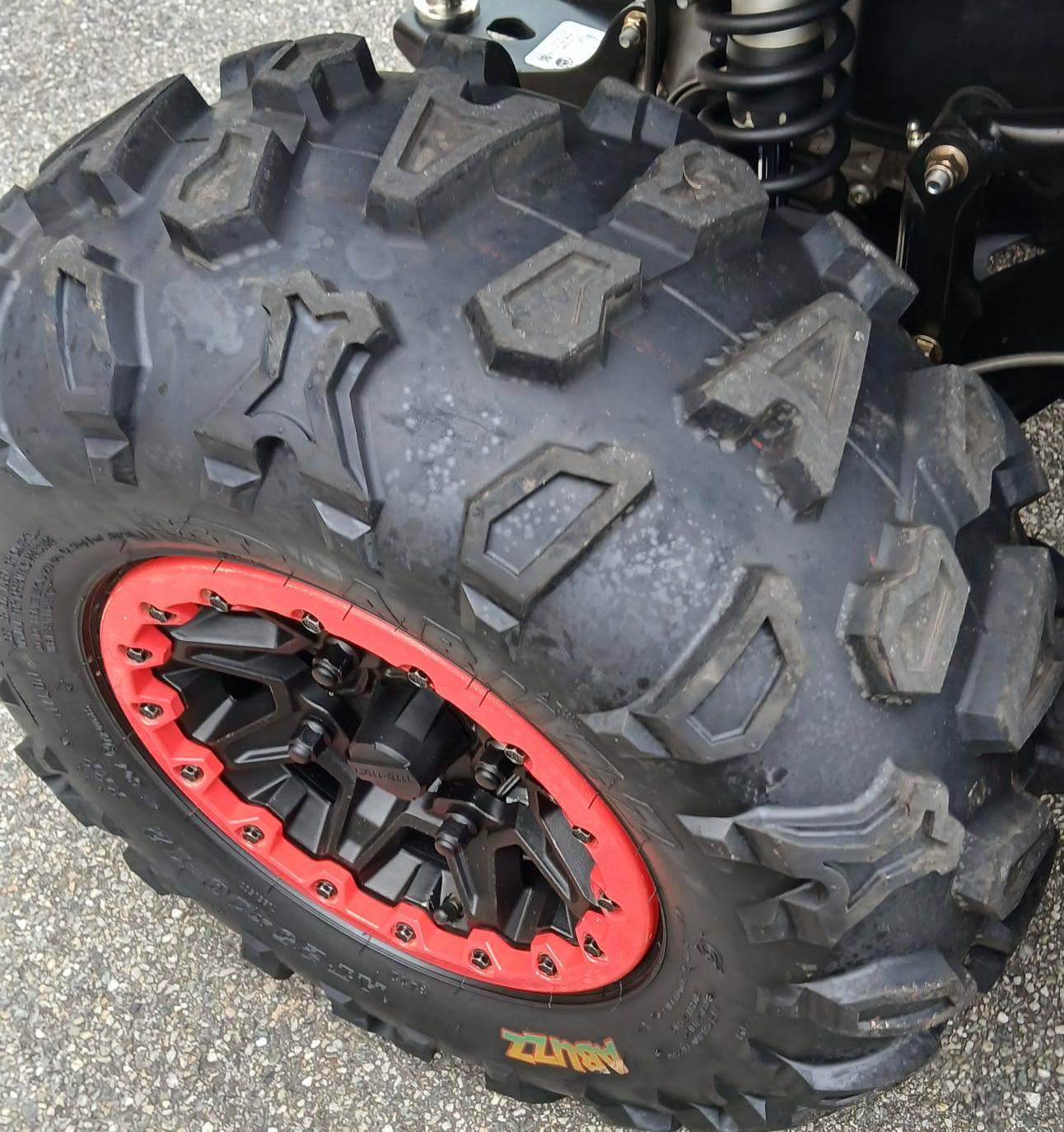 Pneumatico fuoristrada nero con cerchio rosso, primo piano, su asfalto.