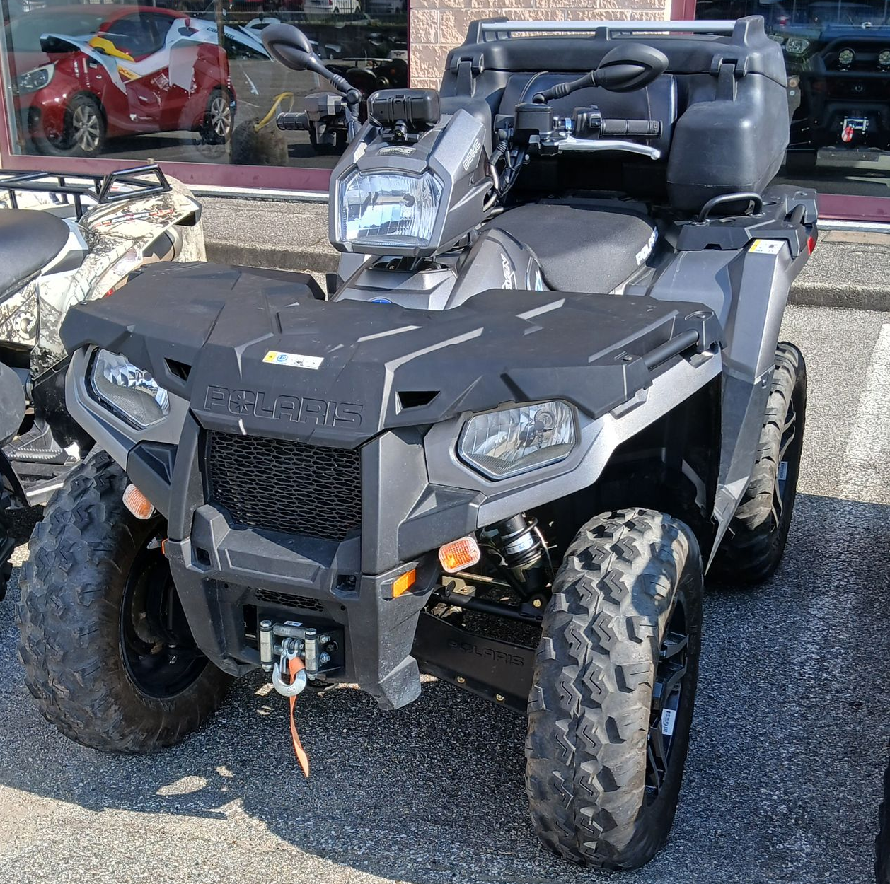 ATV Polaris grigio con pneumatici di grandi dimensioni, vani portaoggetti e verricello anteriore, parcheggiato all'aperto.