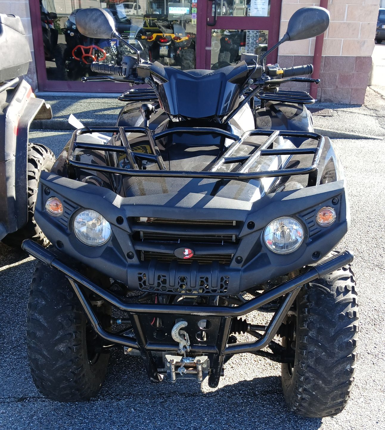 Un quad nero parcheggiato sulla ghiaia davanti a un edificio con porte in vetro e finiture rosse.