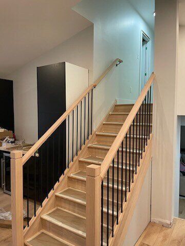 Wooden staircase with black metal spindles and light-colored wood handrails.
