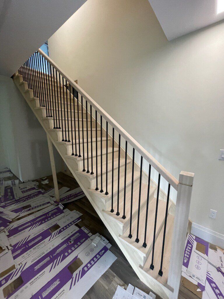 Staircase with light wood steps, black iron balusters, and a neutral-colored wall. Construction materials on the floor.