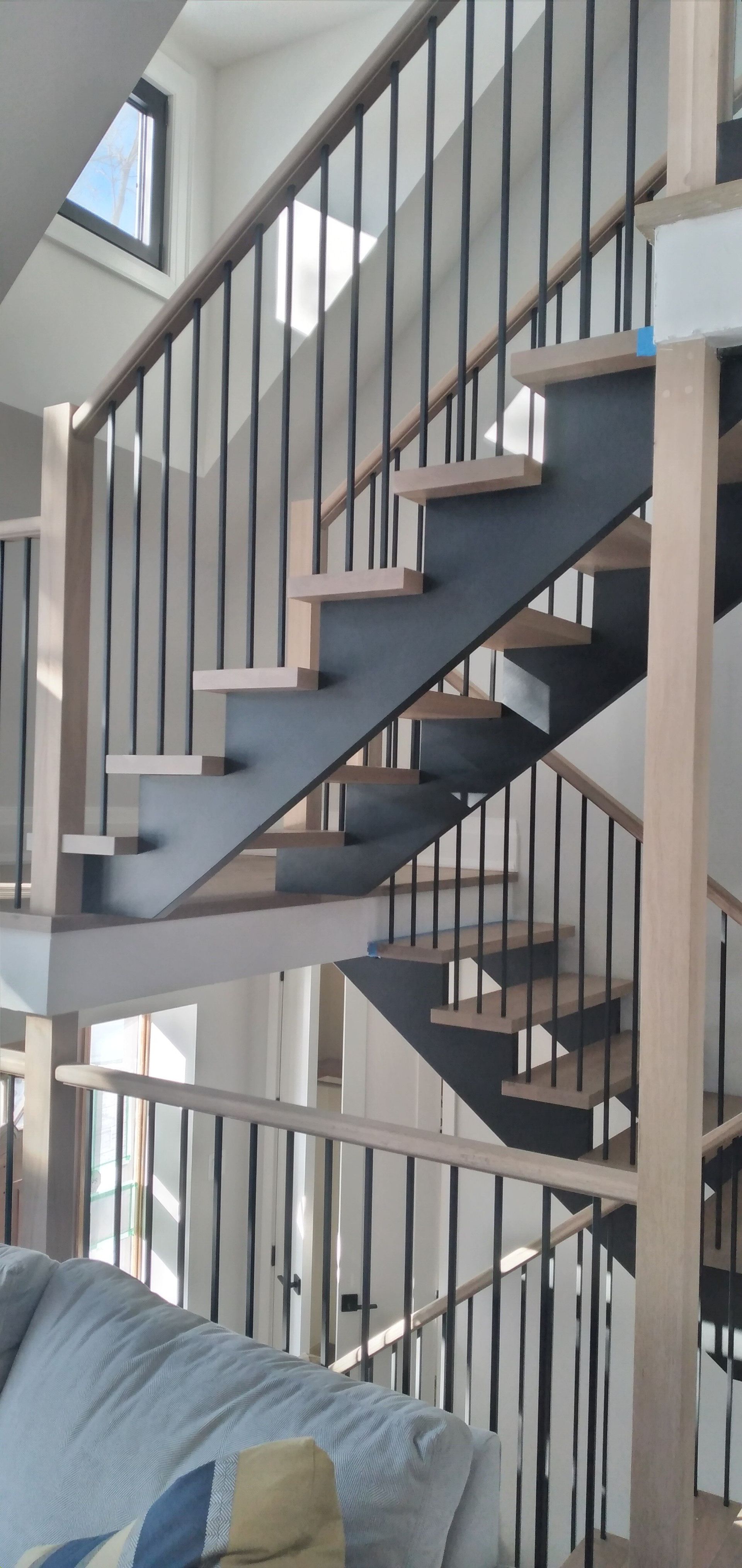 A staircase with wooden steps and black metal railings, light wooden supports, and a couch.