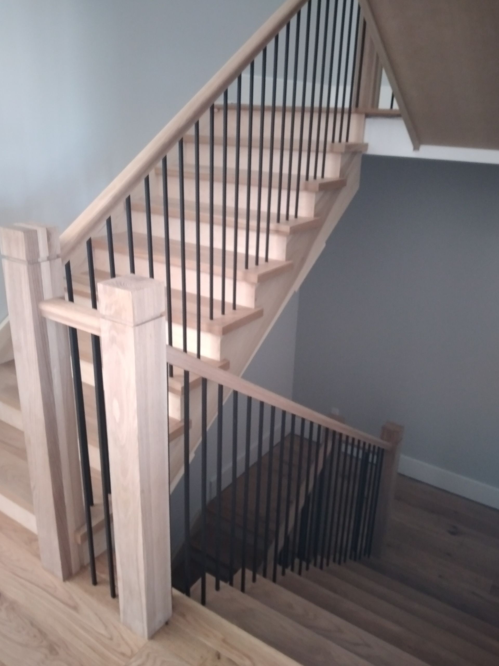 Wooden staircase with light-colored wood, black metal spindles, and gray walls.