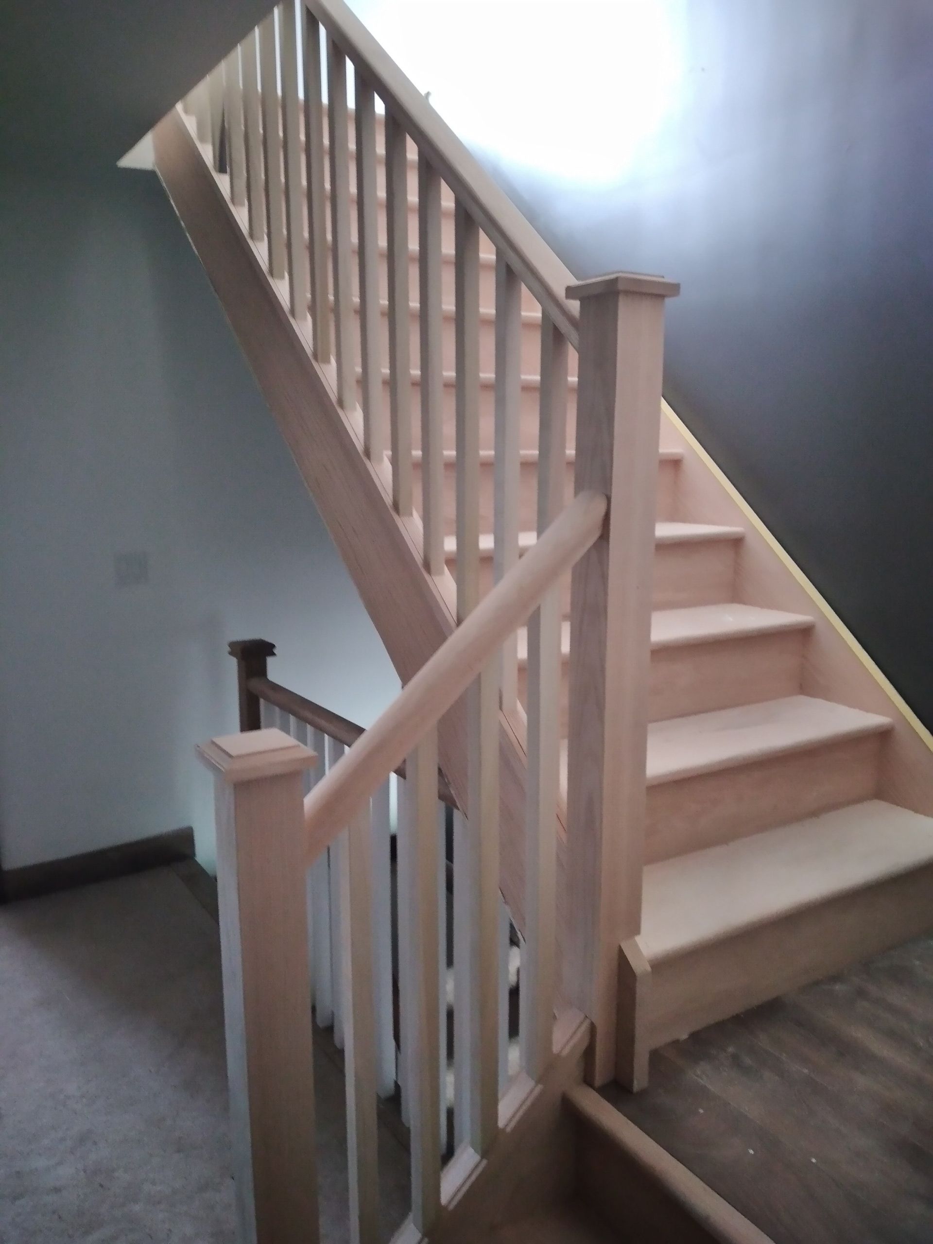 Wooden staircase with banister and railings; neutral walls in the background.