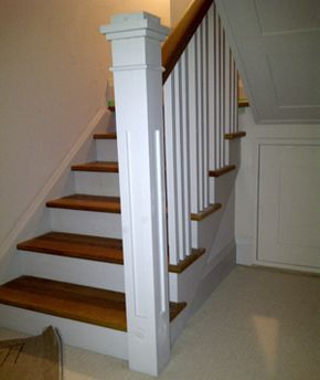 Staircase with wooden steps and white railing, leading upwards. A white post is in the middle.