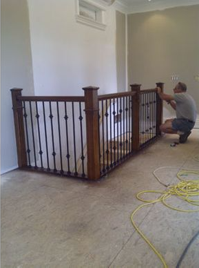 Man installing a wooden and black iron railing on a landing. Wires on floor.