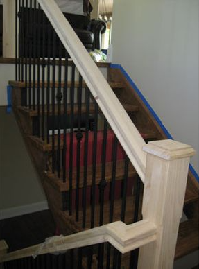 Wooden staircase with black metal spindles and a light-colored handrail; steps are taped and construction is underway.