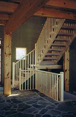 Wooden staircase with light-colored balusters, dark stone floor, and exposed beams.
