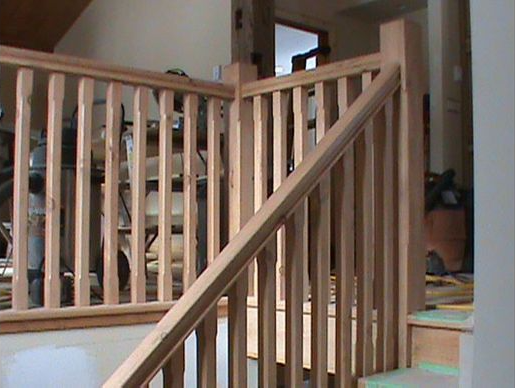 Wooden staircase with railings, indoors. Light wood, vertical balusters, right-hand rail.