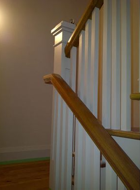 Wooden staircase with white vertical paneling and a wood handrail.