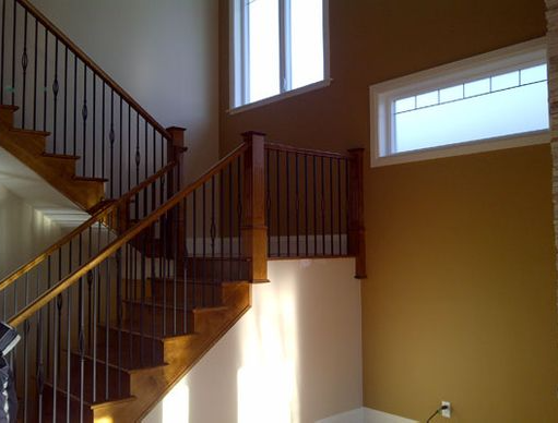 Wooden staircase with black iron railings, leading to a landing with windows on a gold wall.
