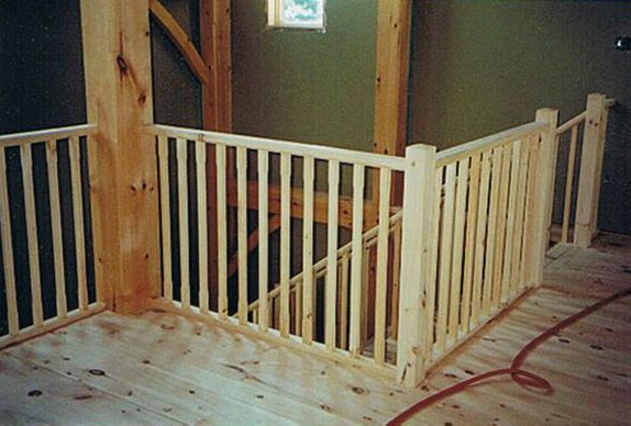 Wooden railing along a staircase landing in a building, light-colored wood.