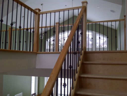 Wooden staircase with black iron spindles, light wood railings, and an open entryway.