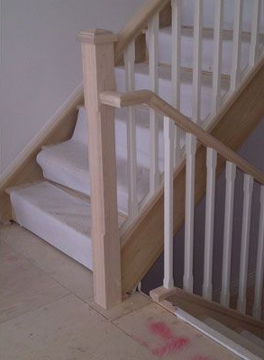 Staircase with light wood and white balusters. The stairs are covered with white padding.