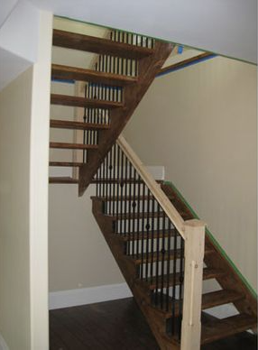 Staircase with wooden steps and black spindles, leading up to a second story, neutral-toned walls.