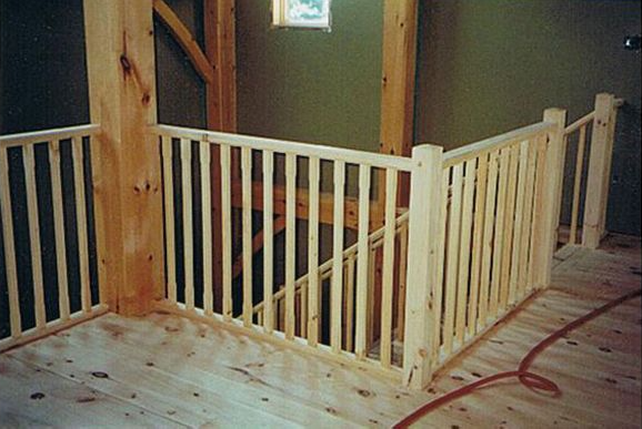 Interior view of a wooden railing surrounding a staircase, with a light green wall and natural wood beams.