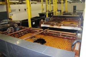 Industrial plating tanks filled with orange spheres, copper piping, and dark liquid.