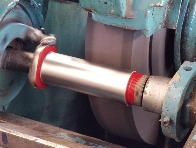 Metal shaft being ground on an industrial machine.