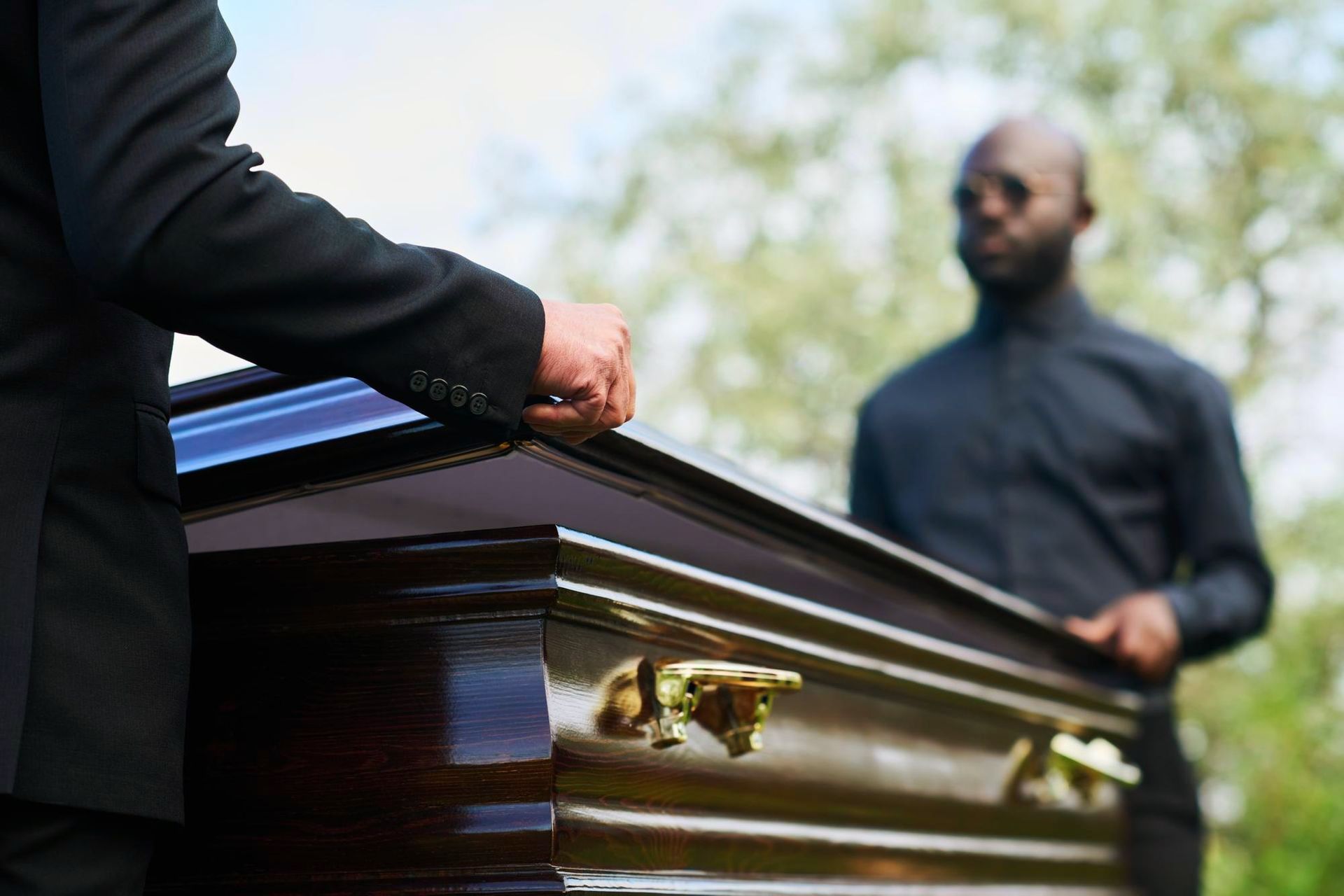 Two men are standing next to a coffin at a funeral.