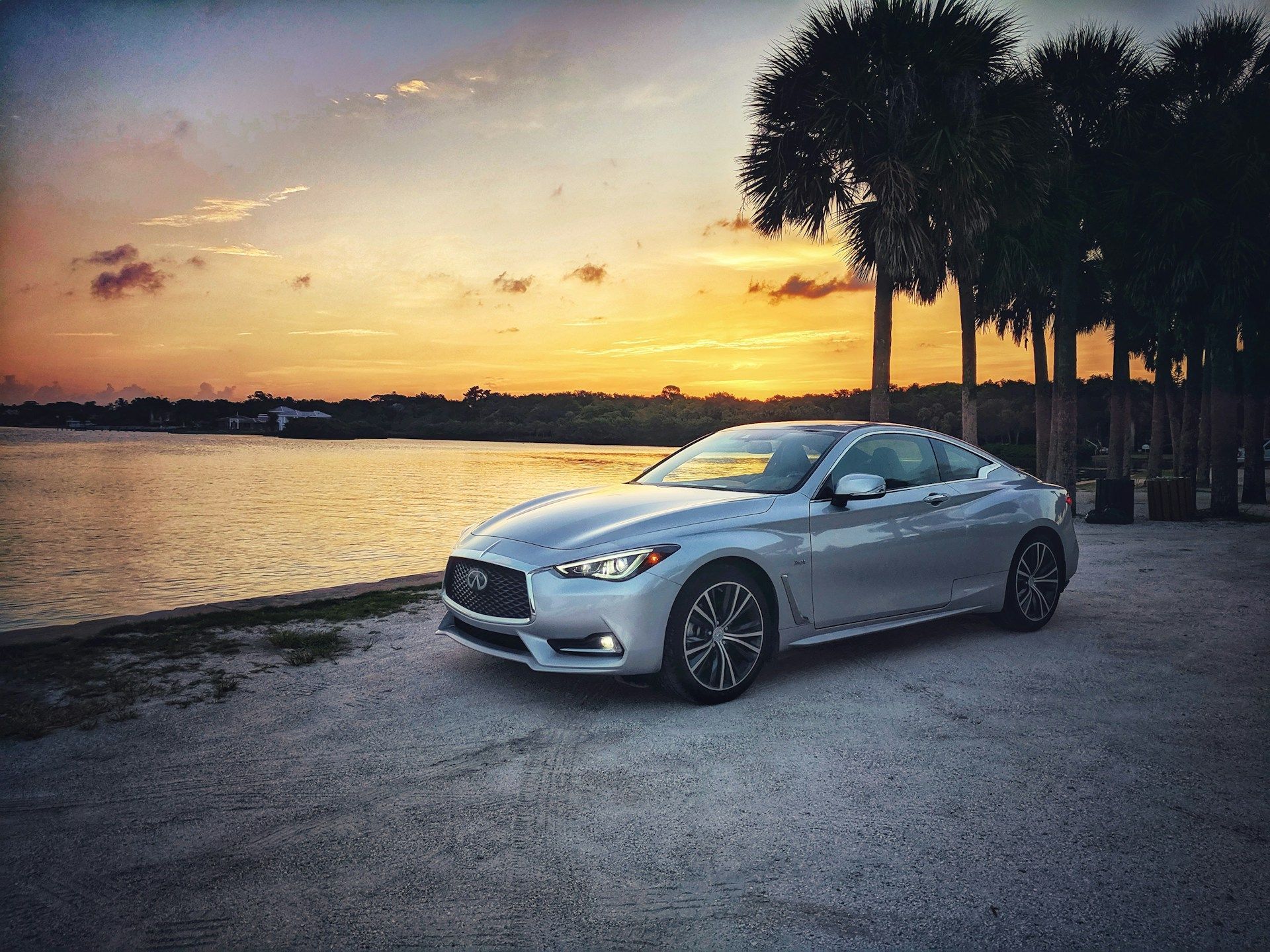 A silver car is parked next to a body of water at sunset.