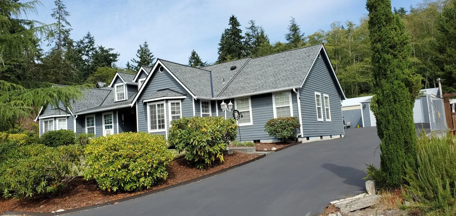 A large house with a gray roof is surrounded by trees and bushes.