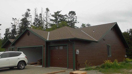 A white car is parked in front of a brown house.