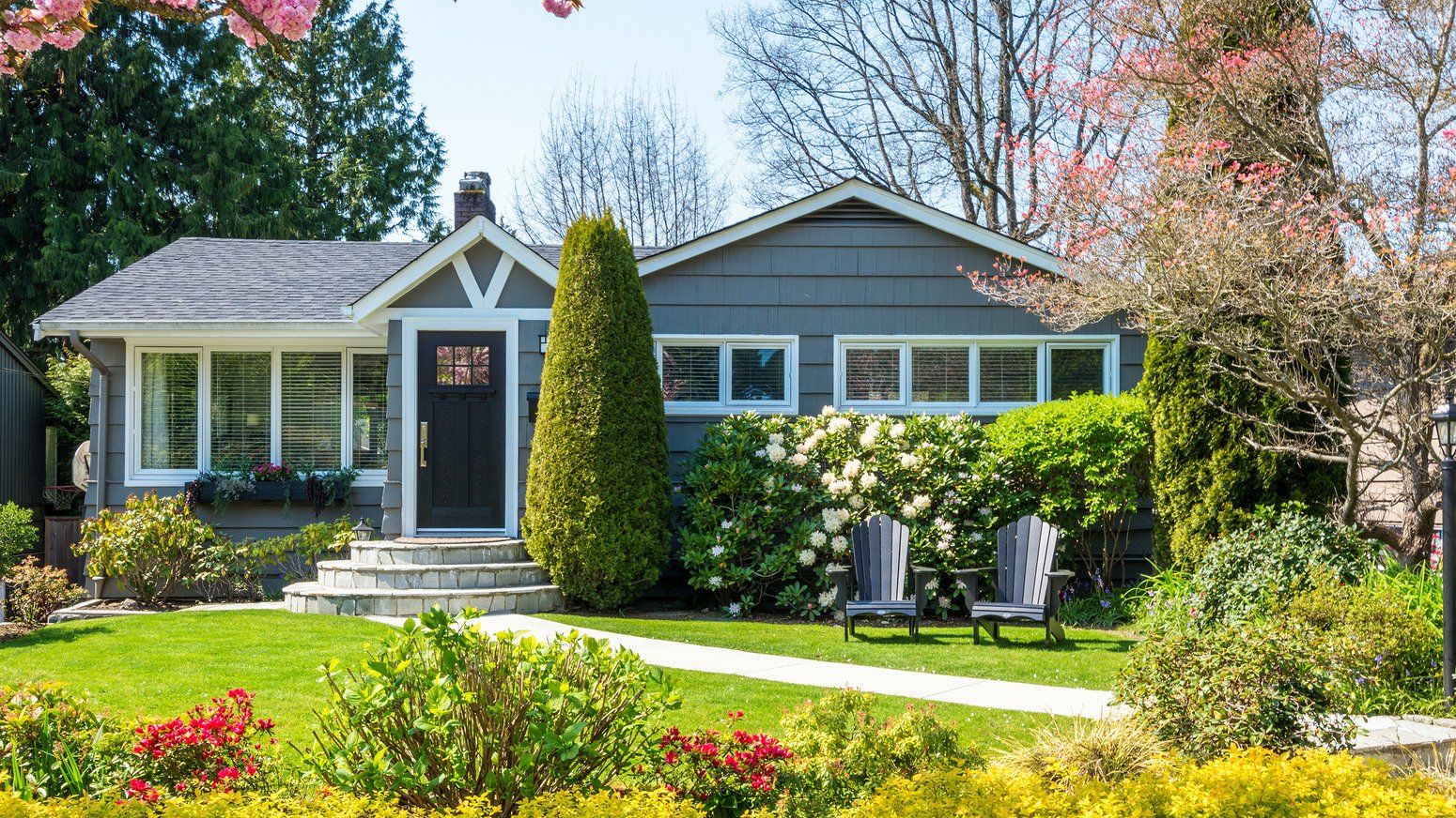 A gray house with a lush green lawn and chairs in front of it.