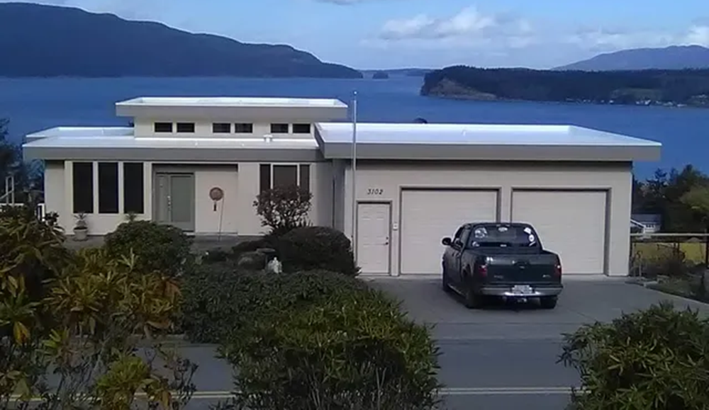 Modern light-colored house with a two-car garage, truck in driveway, water and mountains in background.