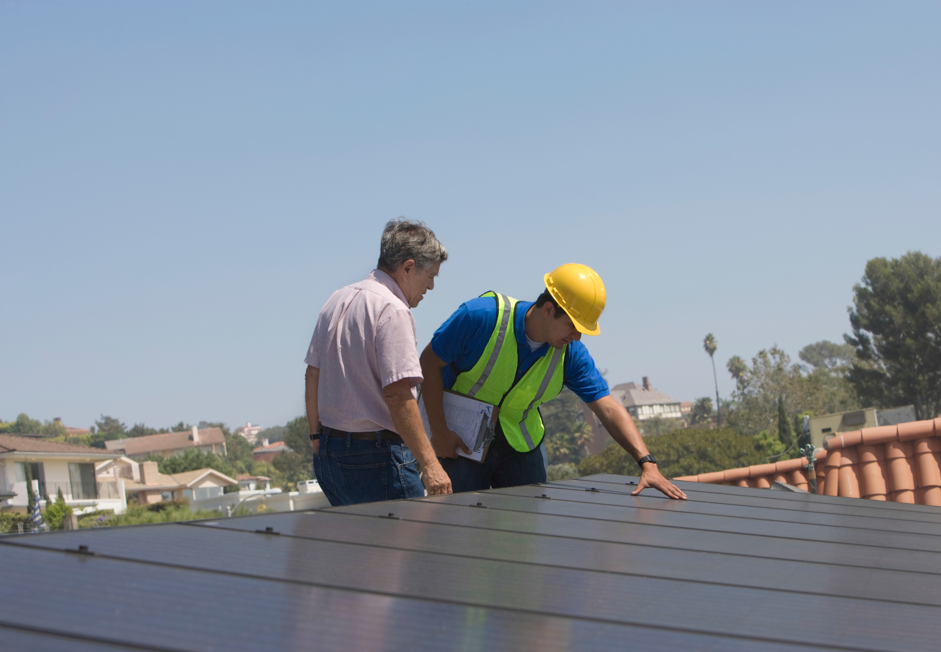 Two men are looking at a solar panel on a roof.