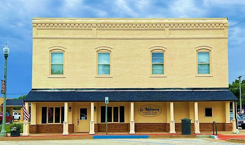 Yellow brick building with a black awning and arched porch. Four windows on the second floor and four small windows on the porch.