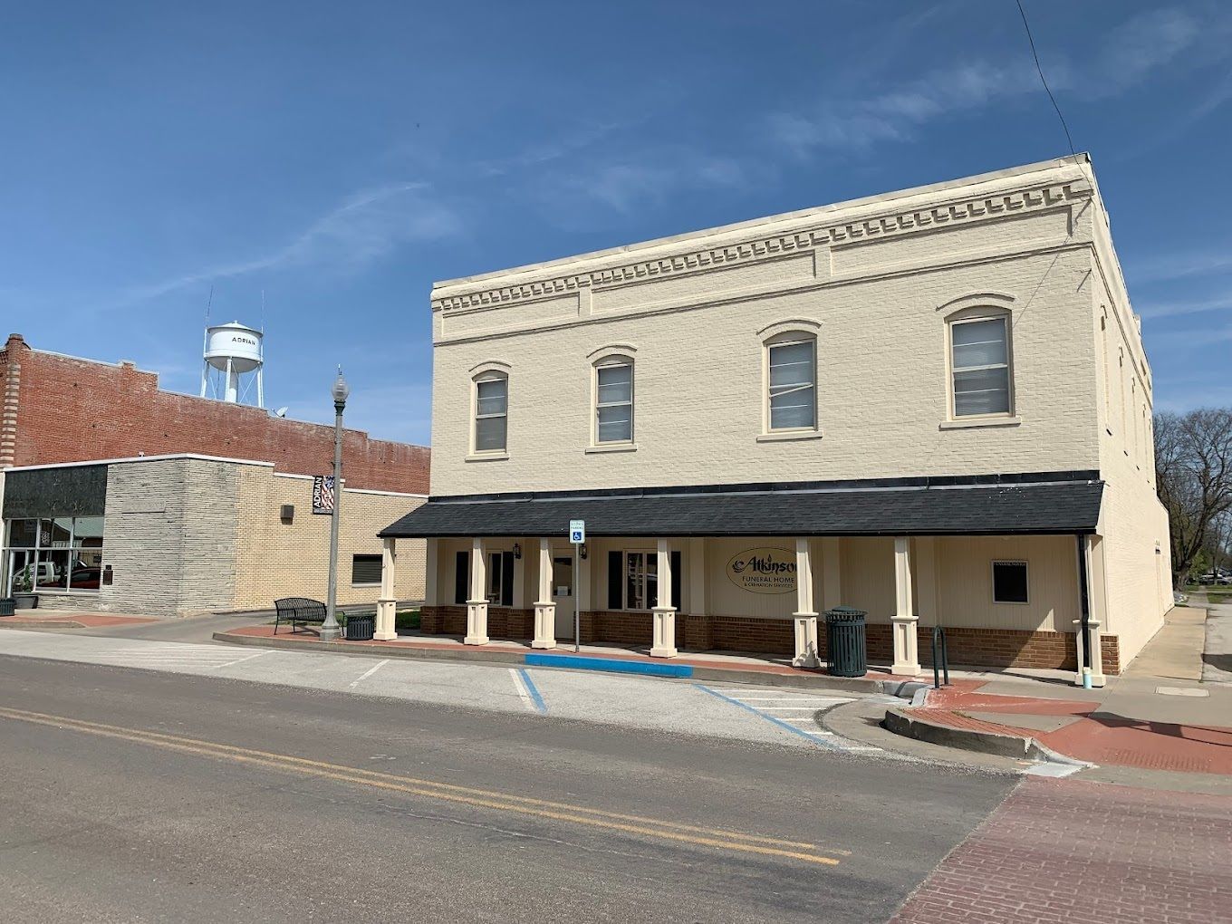 Two-story tan building with a black awning and street in front, with another building and a water tower visible.