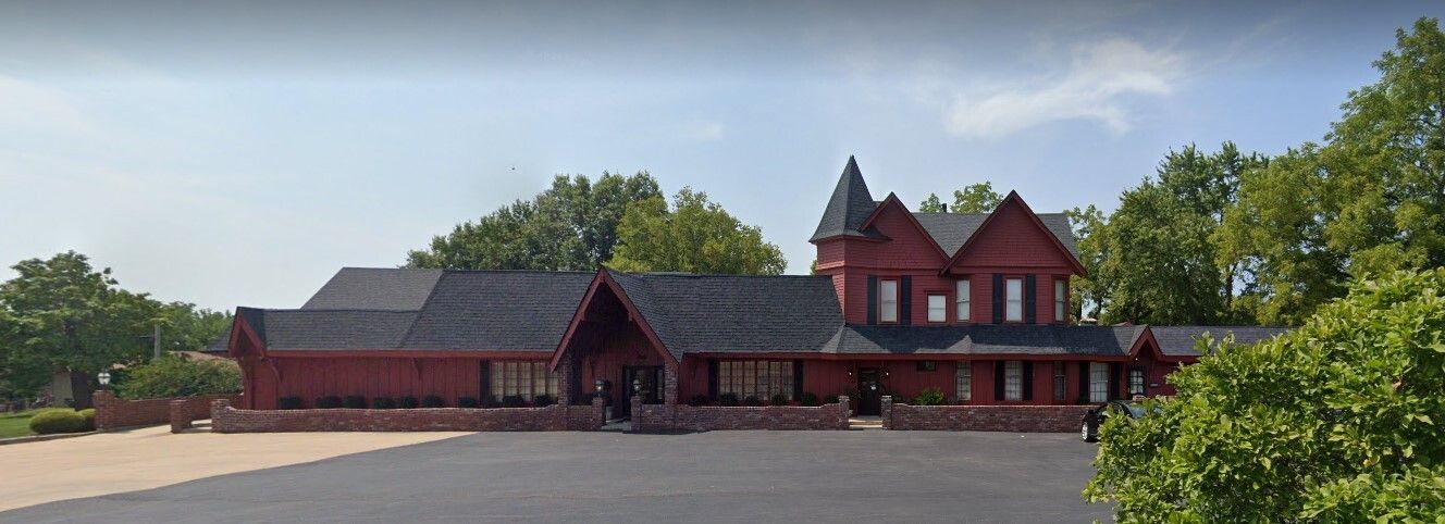 Red Victorian style building with a black roof and a parking lot in front.