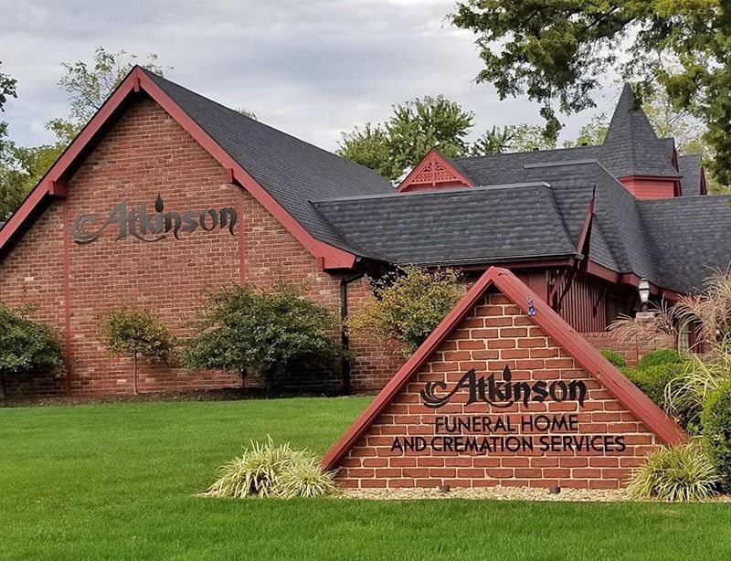 Atkinson Funeral Home, brick building with sign on the lawn. Red roof, green grass, and trees.