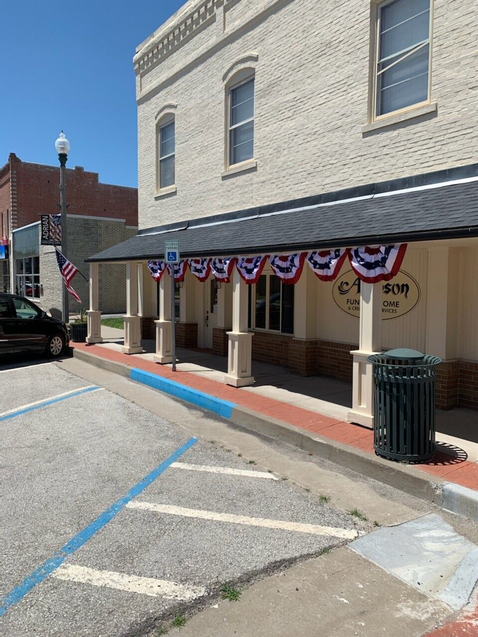A two-story brick building with a covered porch decorated with red, white, and blue bunting.