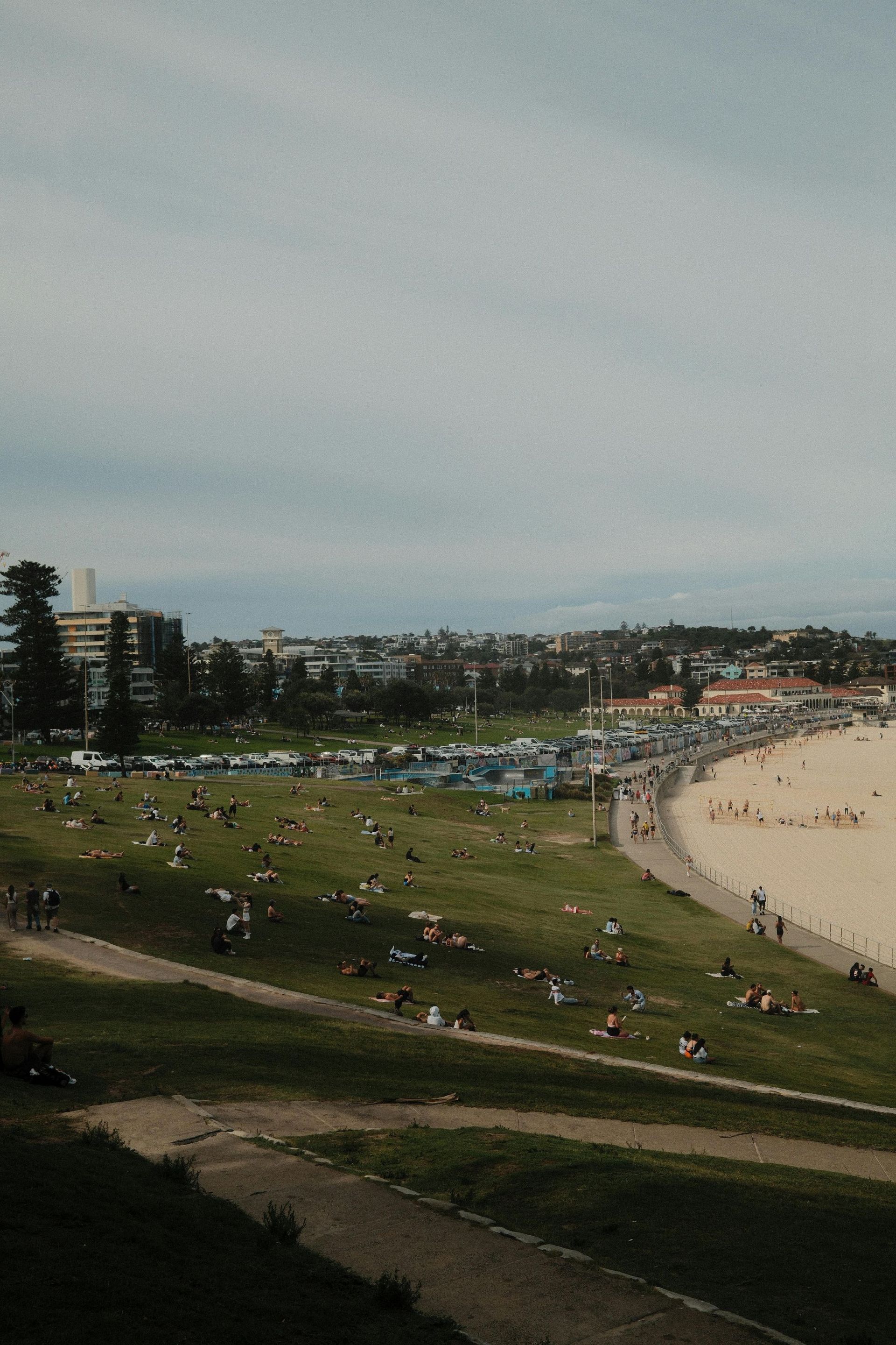 Crowded beach and grassy park by the shoreline on an overcast day