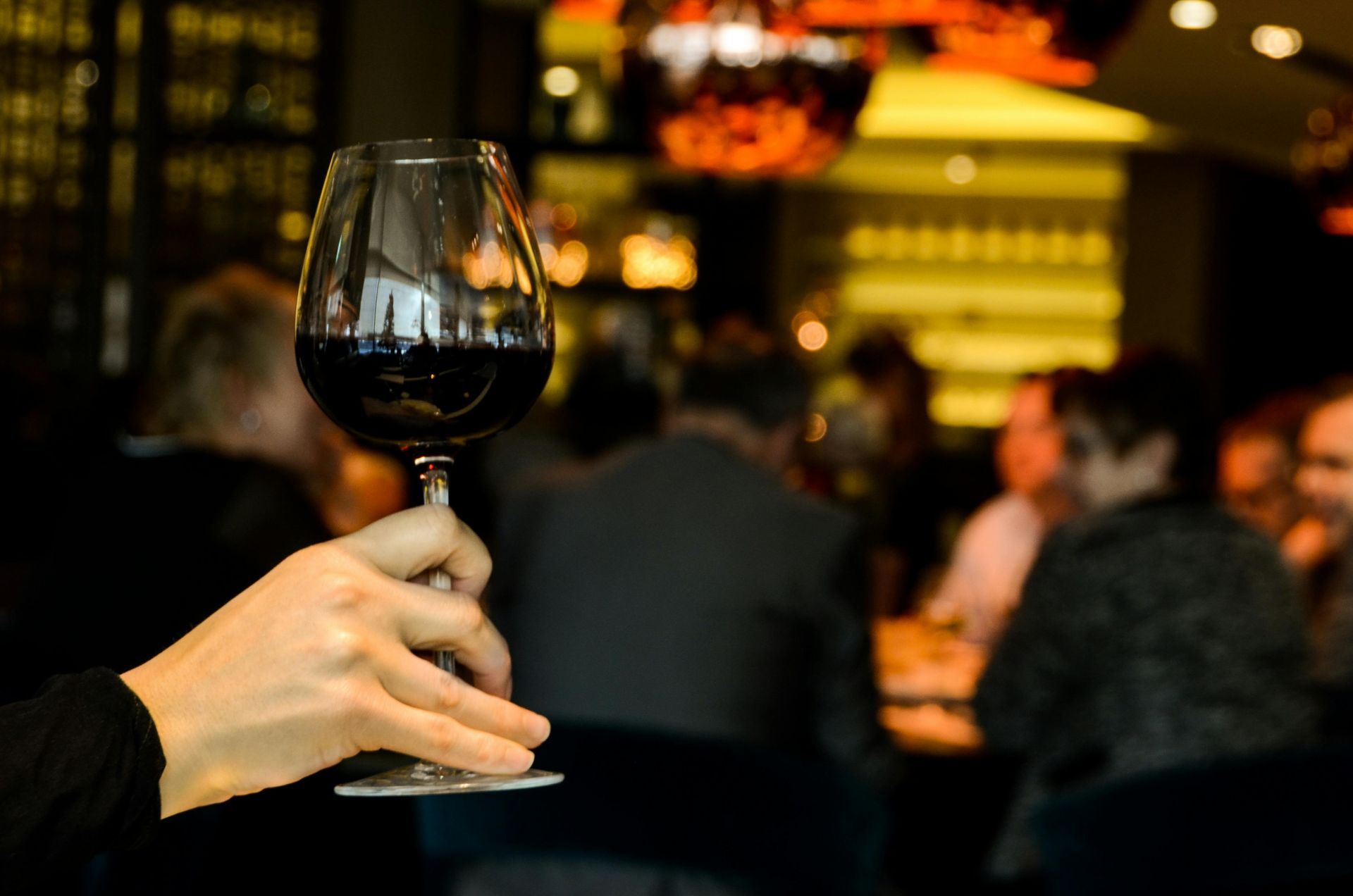 Hand holding a glass of red wine in a dimly lit bar or restaurant.