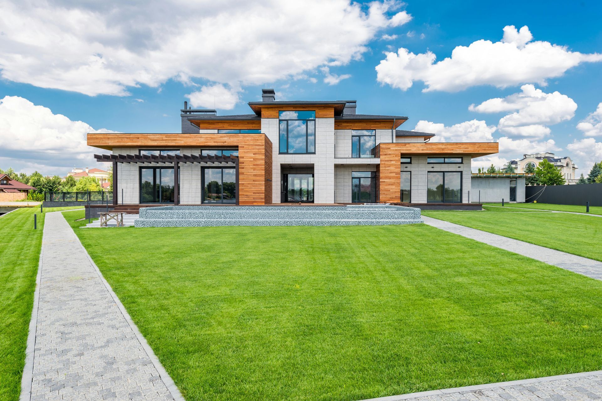 Modern two-story house with large windows, stone accents, and a manicured green lawn under a partly cloudy sky