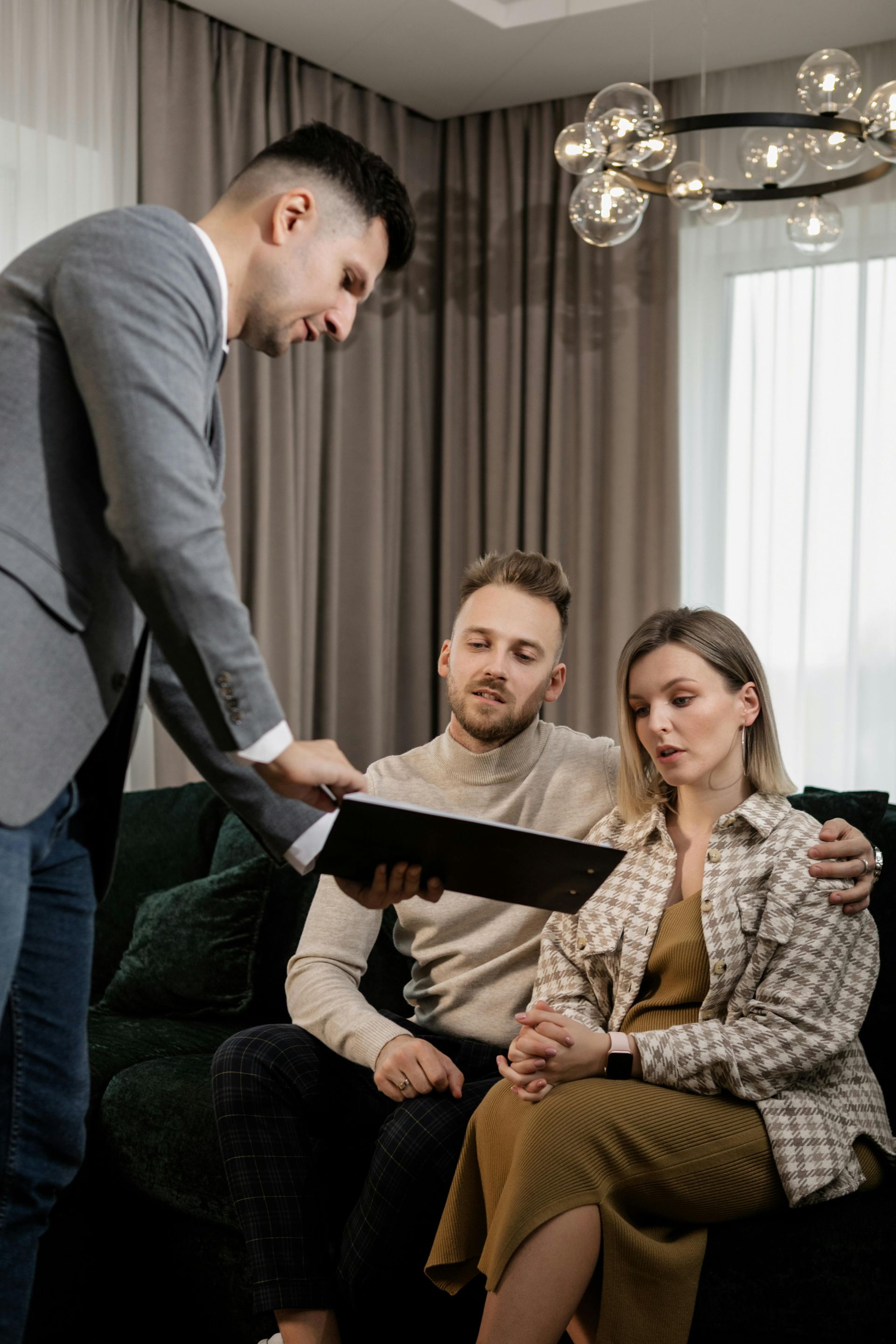 A realtor showing a folder to two seated clients in a modern living room