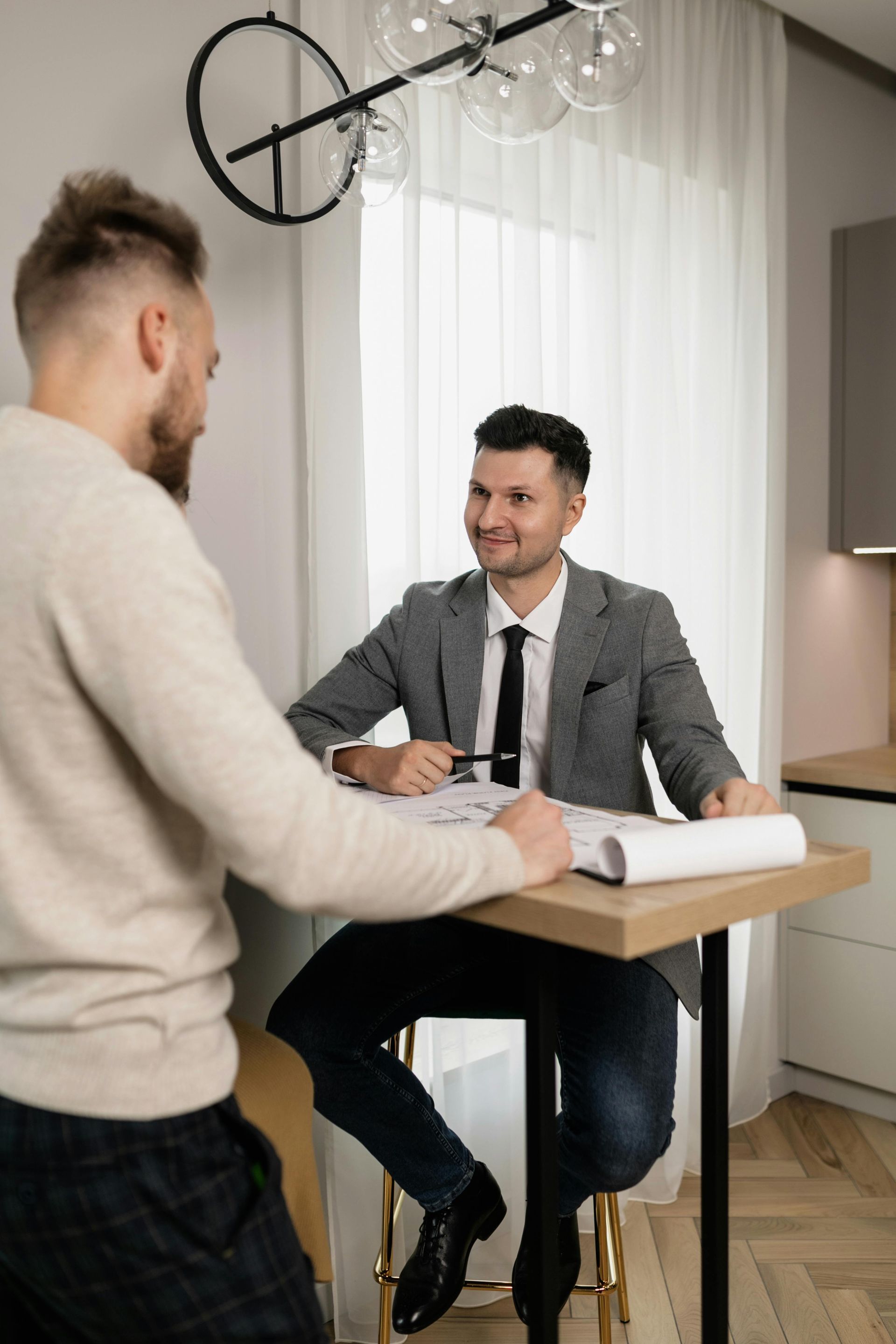 Two men meeting at a desk in a bright office, one taking notes while the other smiles.
