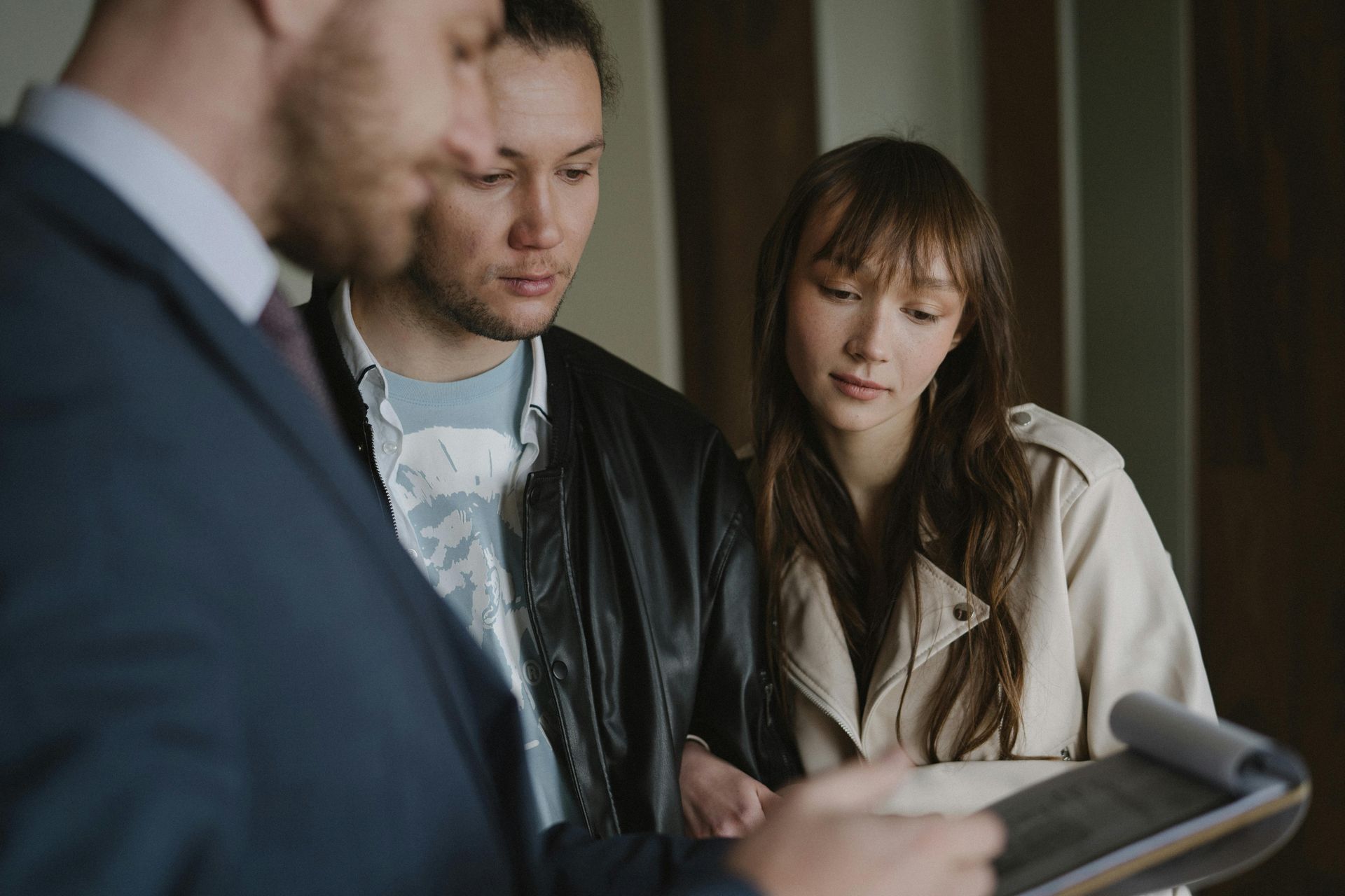 Three people in a meeting looking at a tablet, one man gesturing while others listen attentively.