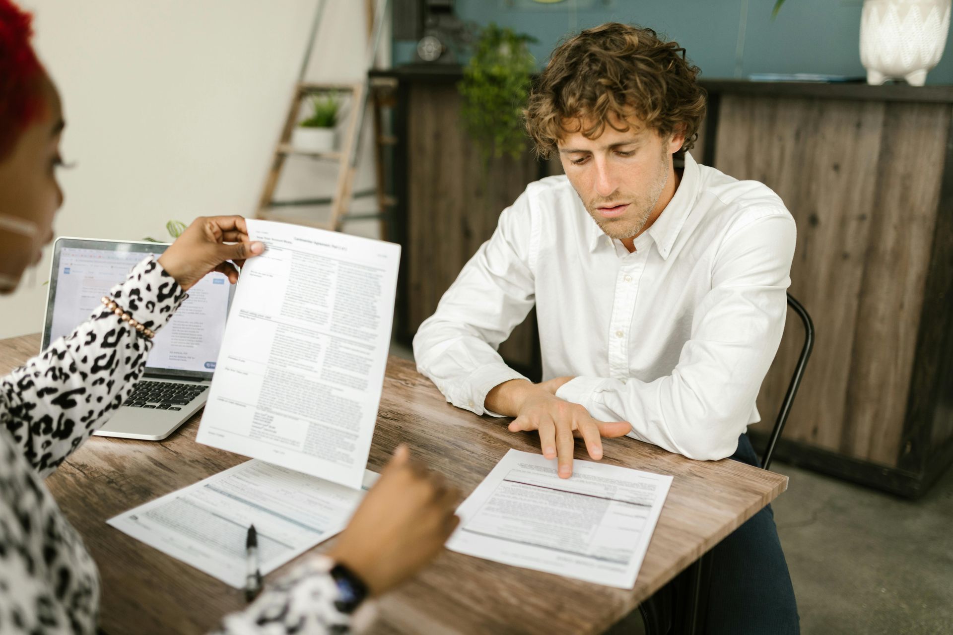 Two people reviewing documents at a wooden table in a bright office or café