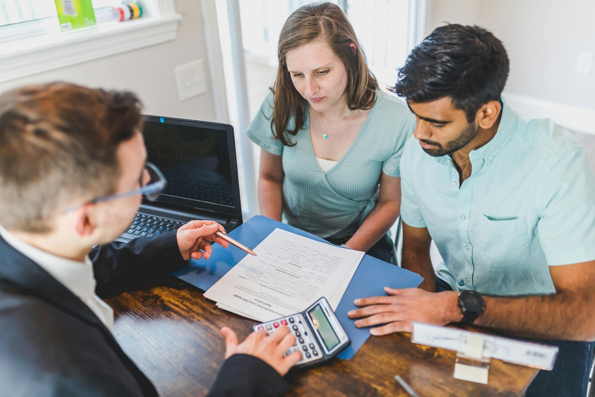 Three people review paperwork and a calculator during a business meeting at a desk.