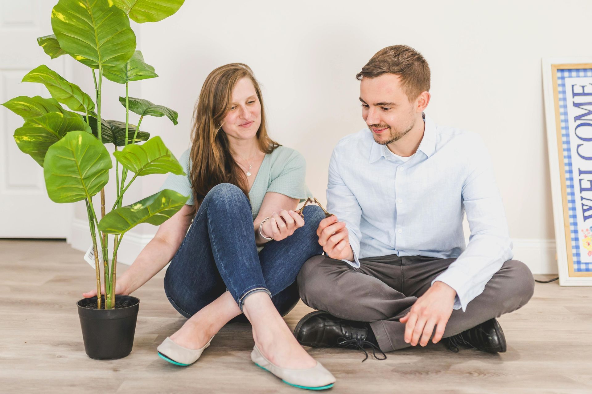 a couple sitting on the floor, both holding out house keys.