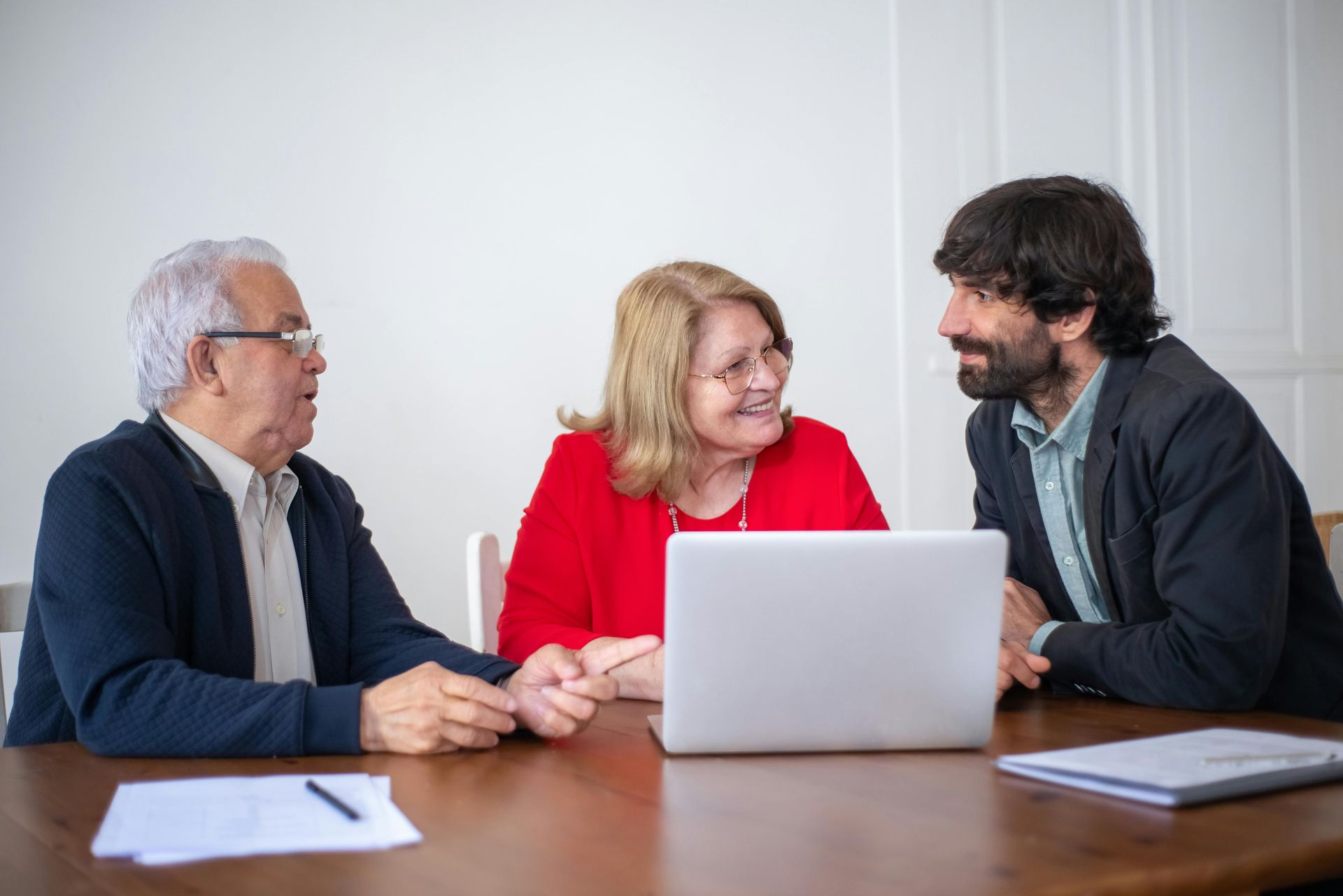 Three colleagues in a meeting around a laptop, smiling and talking at a conference table.