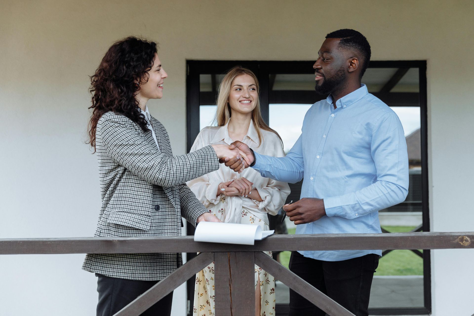 Three colleagues shaking hands on a balcony in front of an office building