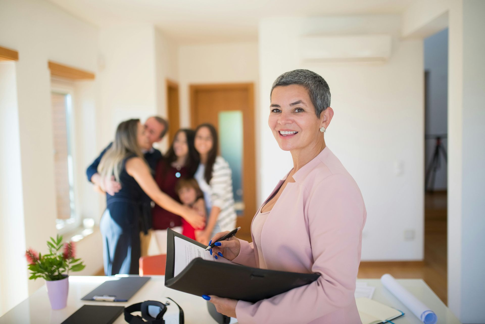 Woman holding a folder in a bright office while three people greet each other in the background