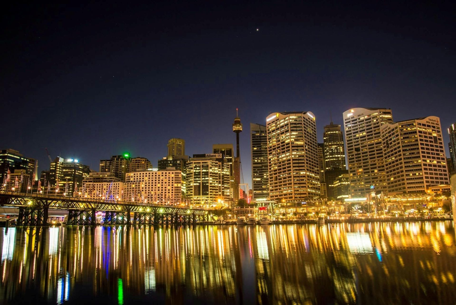 Night skyline of illuminated high-rise buildings reflecting on calm water at dusk