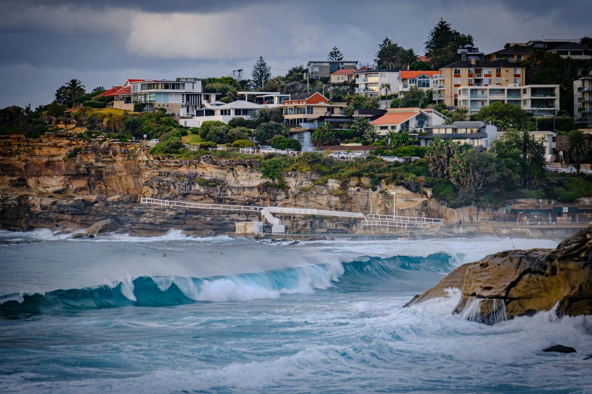Waves crashing below seaside cliffs with homes and apartments overlooking the coast