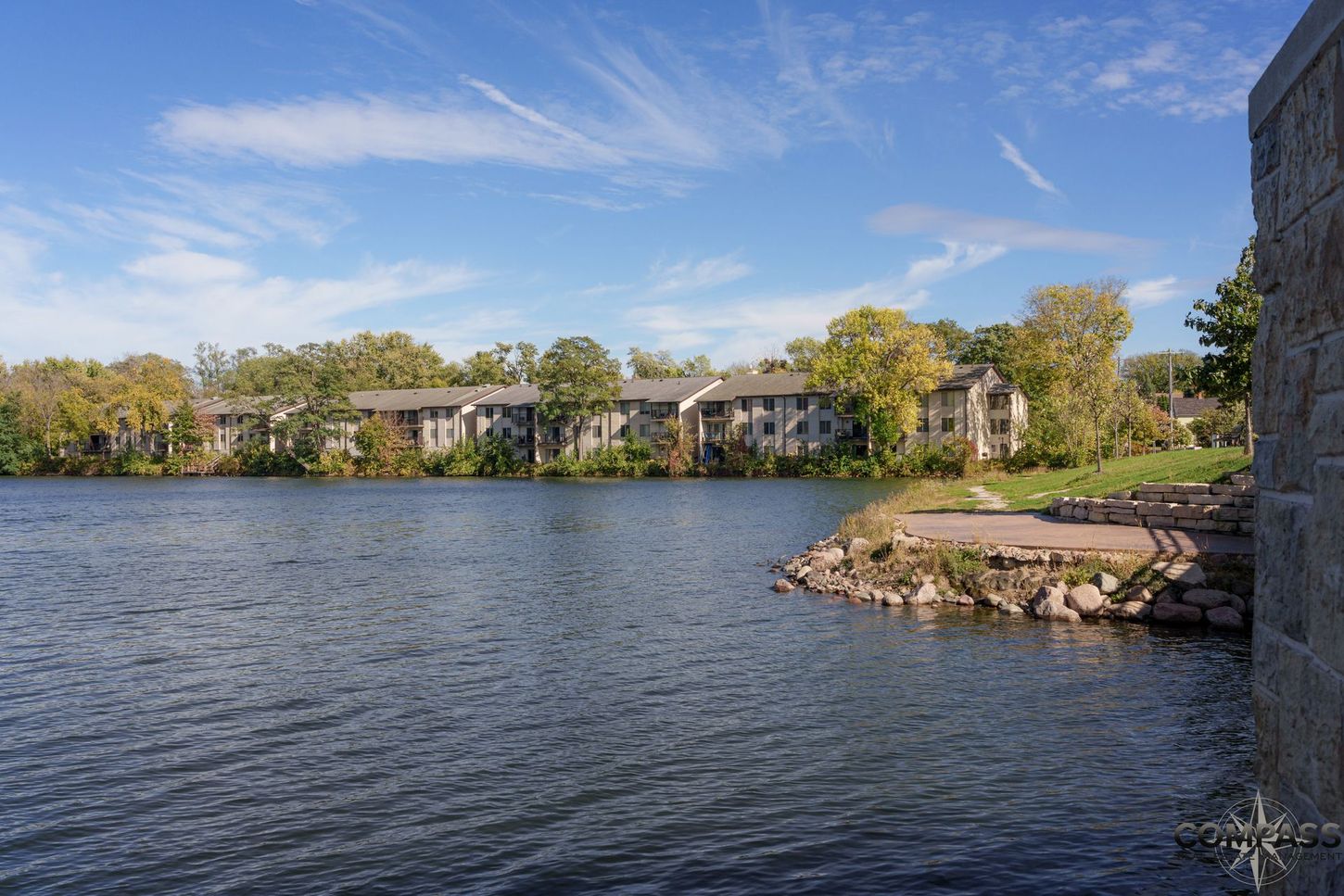 Lake with rippling water and lakeside apartment buildings under a blue sky