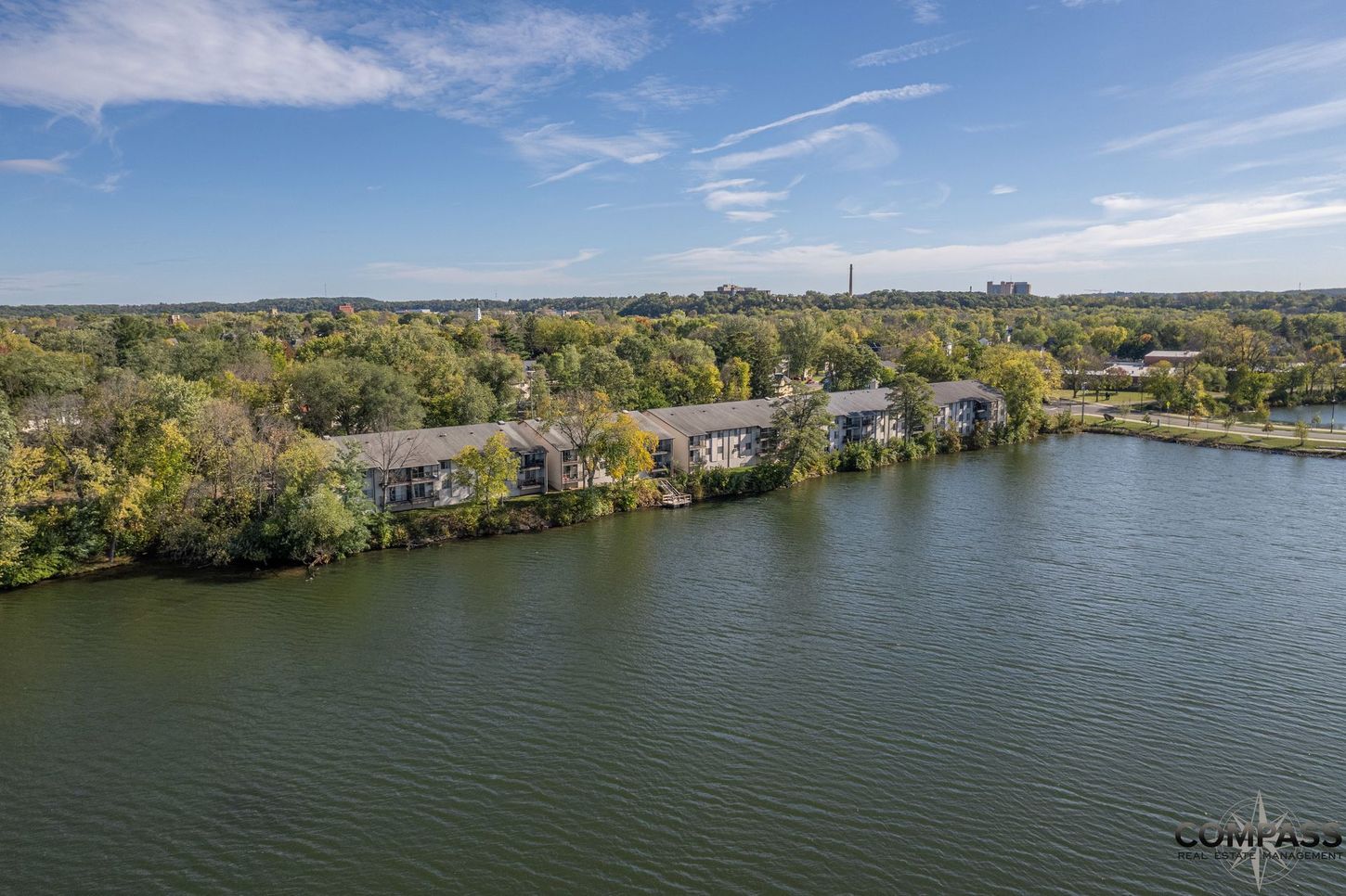 Aerial view of a lakeside park with trees, a shoreline path, and calm water under a clear sky
